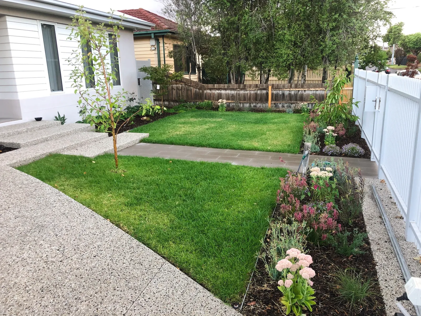 Exposed aggregate concrete driveway and path framing a new front lawn and a flowering garden bed