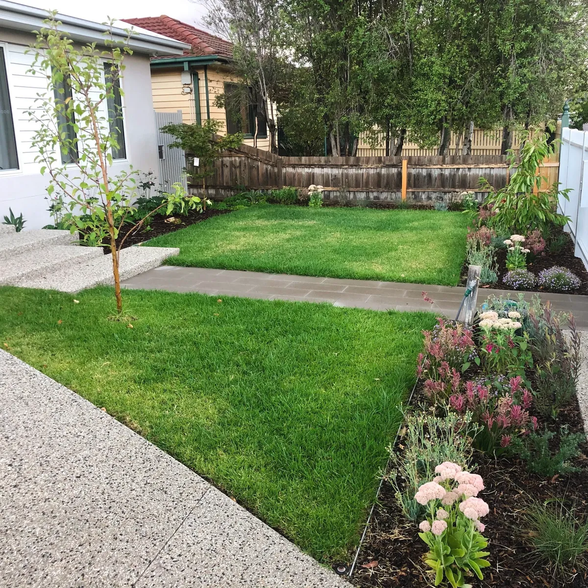 Exposed aggregate concrete driveway and path framing a new front lawn and a flowering garden bed