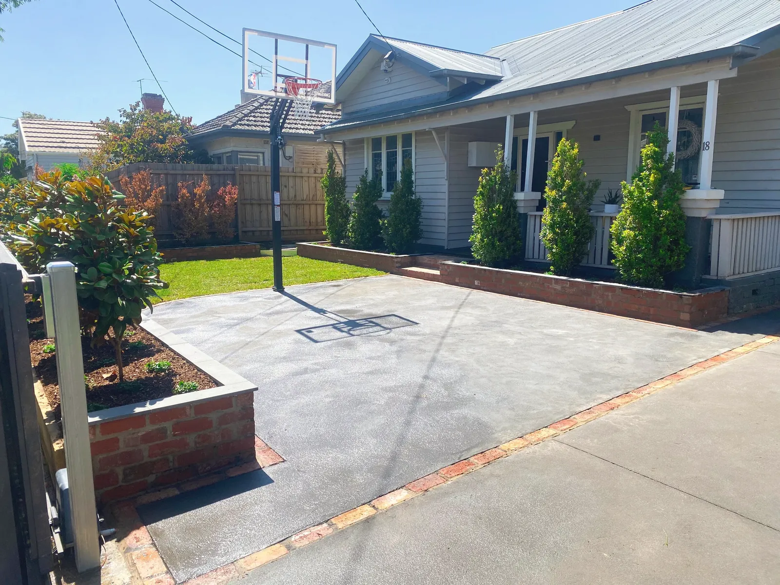 Concrete slab and driveway poured across a front yard, edged with brick garden beds in front of a weatherboard house