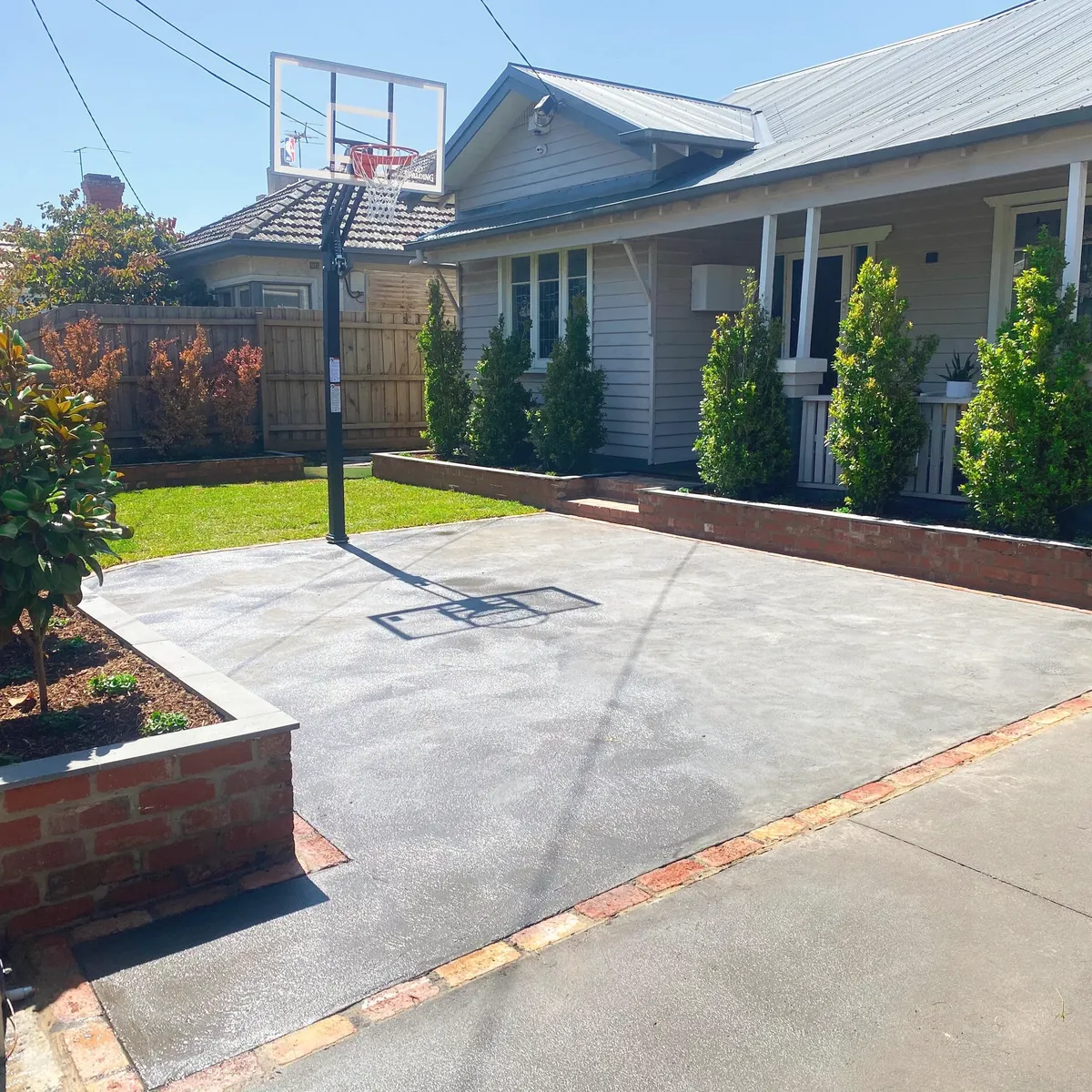 Concrete slab and driveway poured across a front yard, edged with brick garden beds in front of a weatherboard house