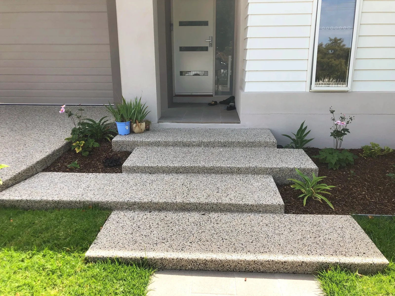 Exposed aggregate concrete entry steps and path leading to a front door, garden beds either side