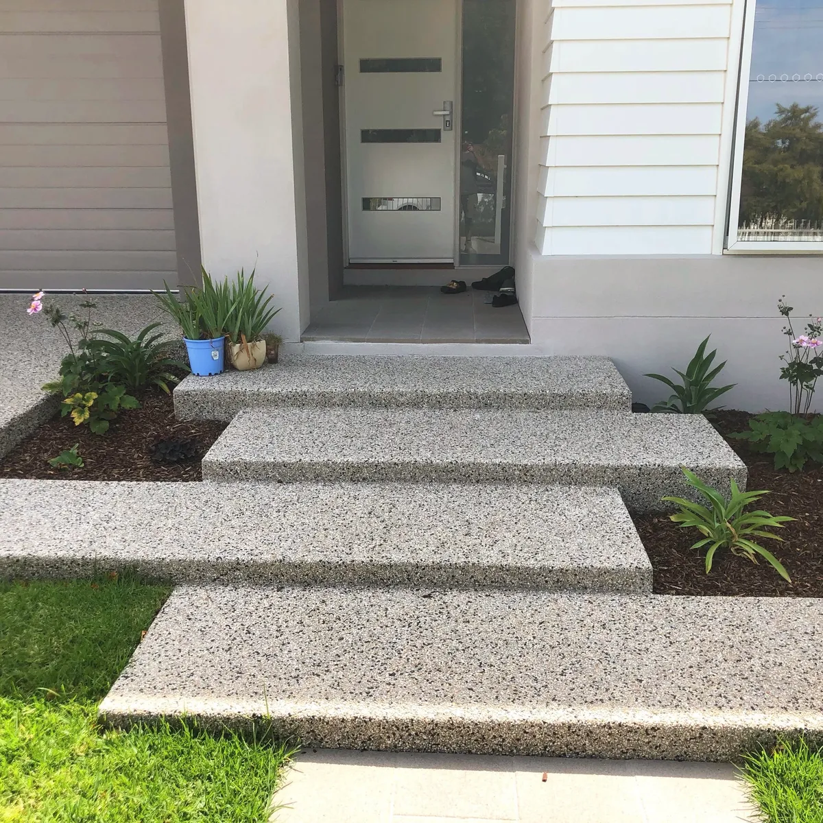 Exposed aggregate concrete entry steps and path leading to a front door, garden beds either side