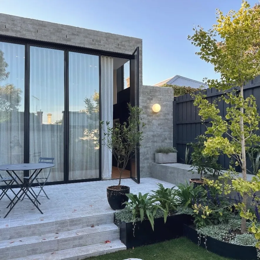Brick garden pavilion with full-height glazing, limestone paving and steps, raised planters and a young tree