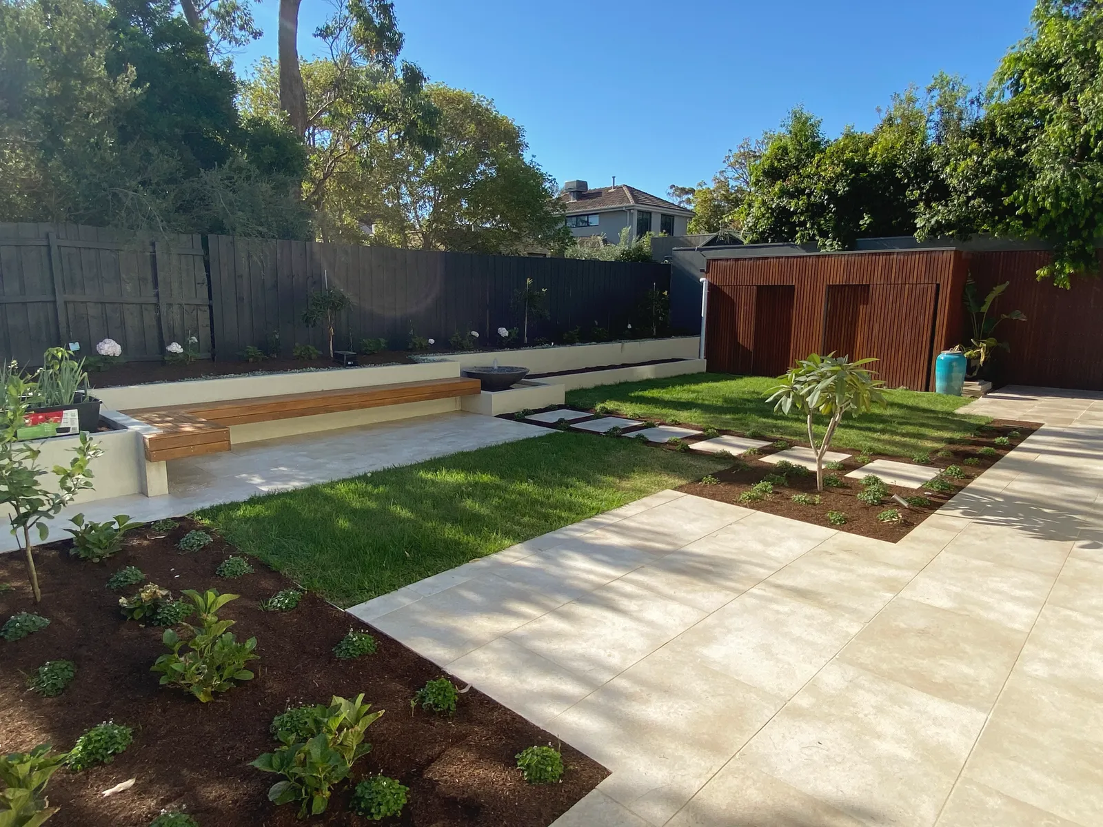 Backyard with a rendered bench seat and timber top, new lawn, large-format paving and freshly planted garden beds