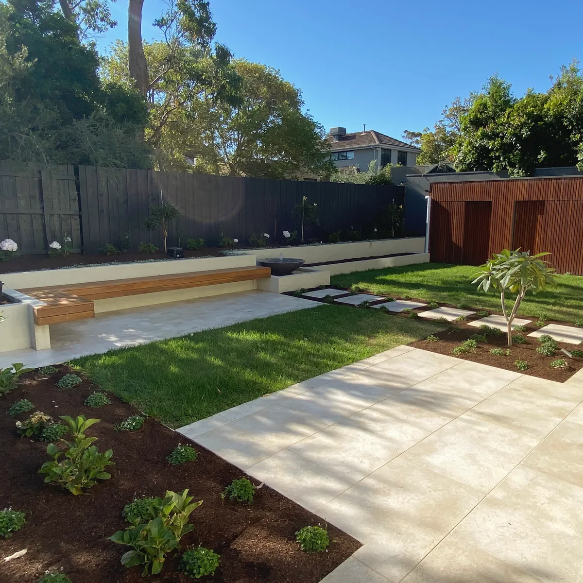 Backyard with a rendered bench seat and timber top, new lawn, large-format paving and freshly planted garden beds
