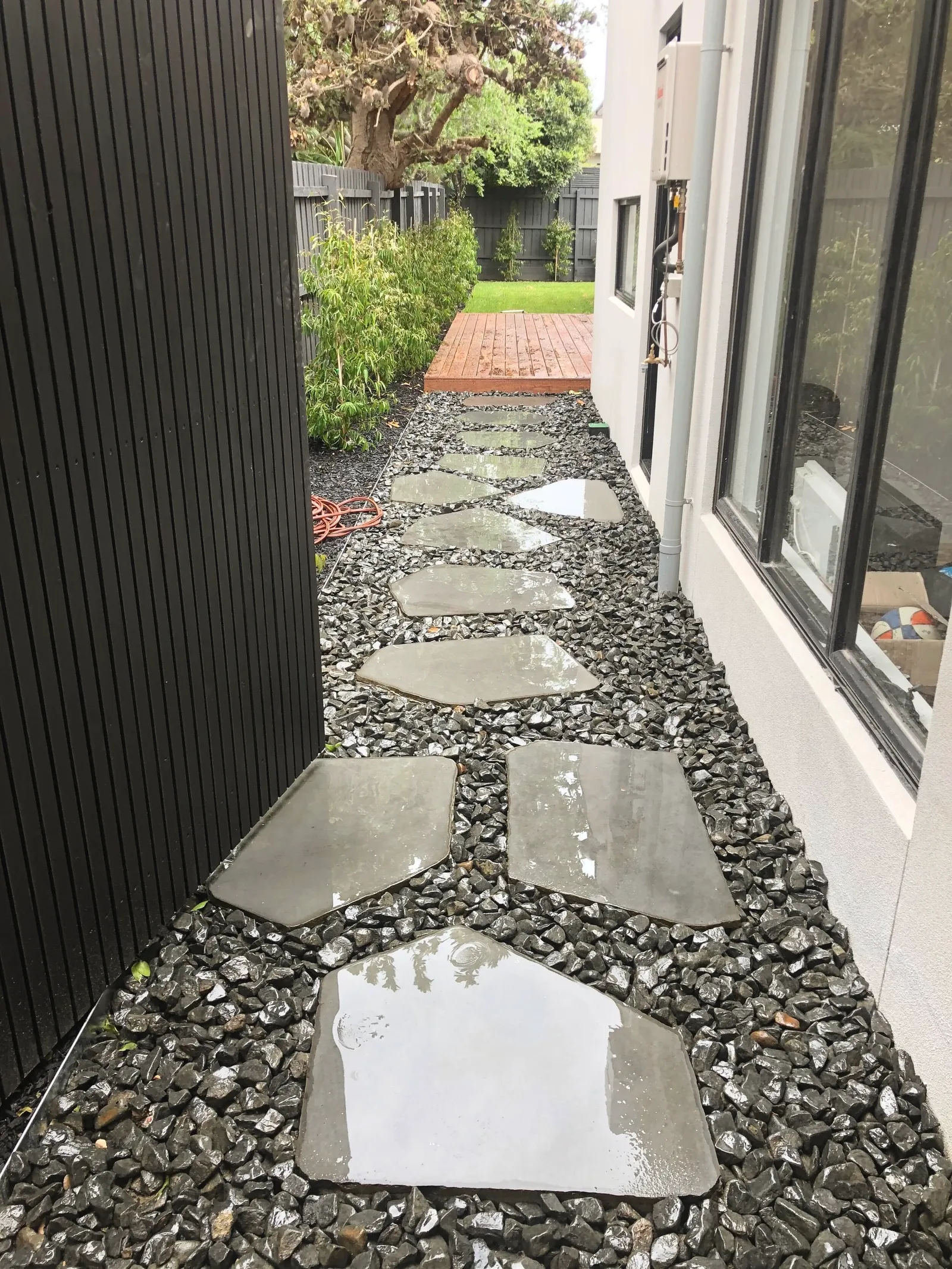 Irregular bluestone stepping stones set into black pebble along a side path, running to a timber deck