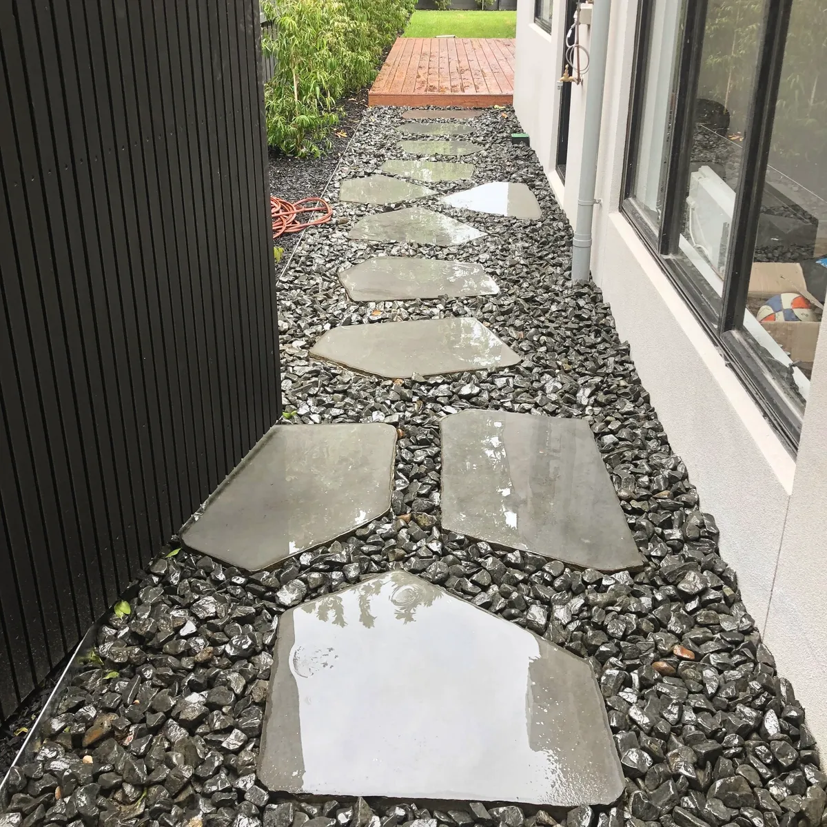 Irregular bluestone stepping stones set into black pebble along a side path, running to a timber deck