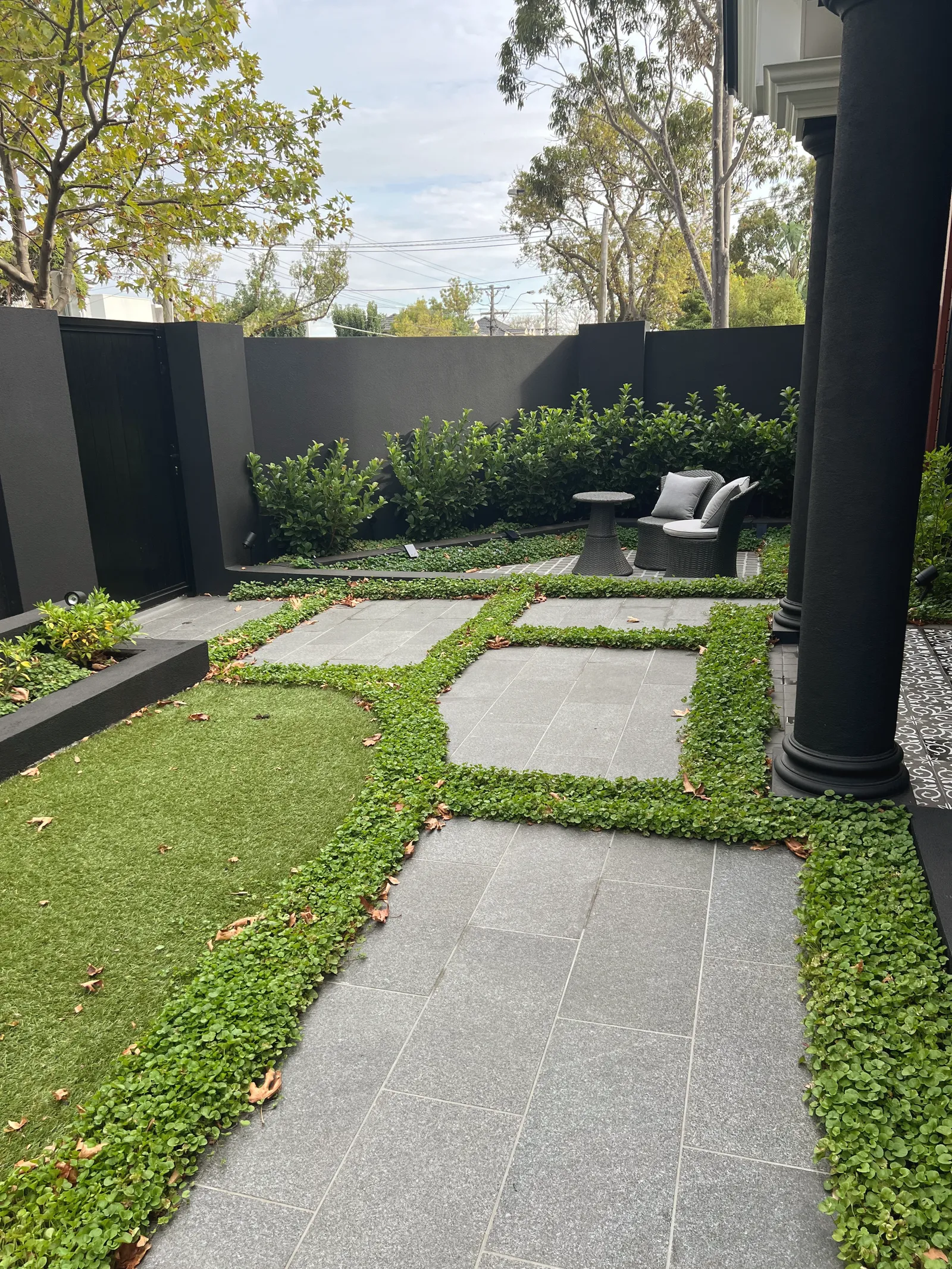 Large granite pavers set into a dichondra groundcover with a sweep of lawn, black screen fencing and a seat at the far end