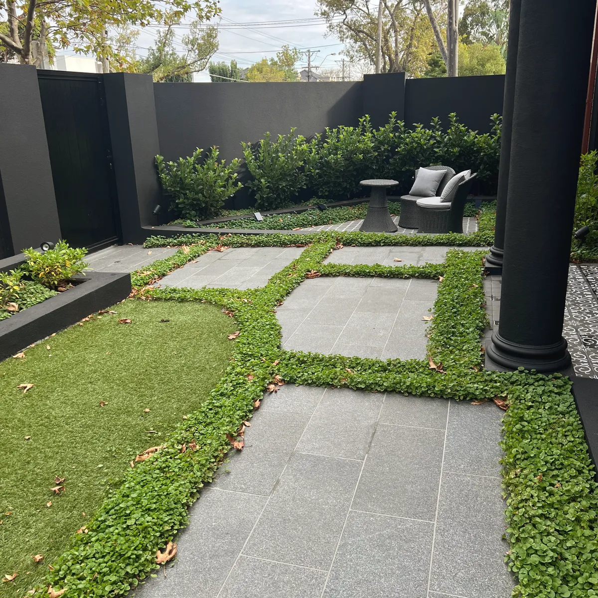 Large granite pavers set into a dichondra groundcover with a sweep of lawn, black screen fencing and a seat at the far end