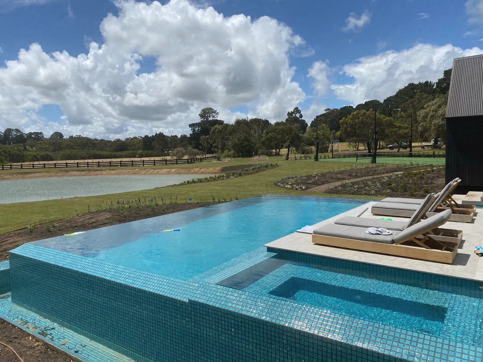 Infinity-edge pool with blue mosaic tiling and a spa, looking out over a dam and paddocks