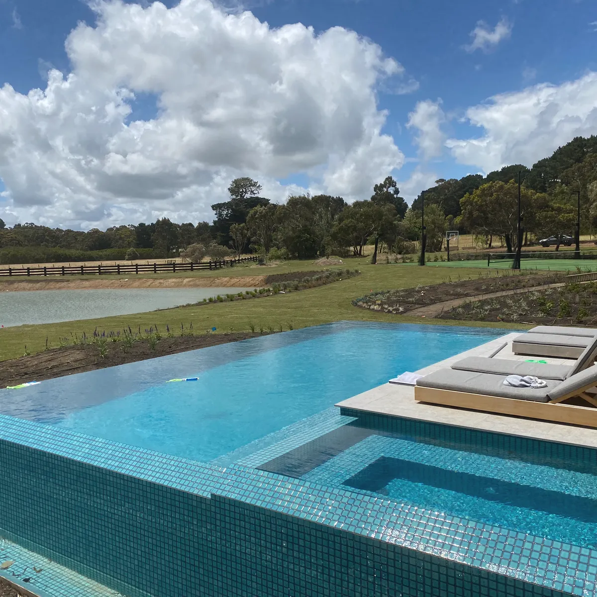 Infinity-edge pool with blue mosaic tiling and a spa, looking out over a dam and paddocks
