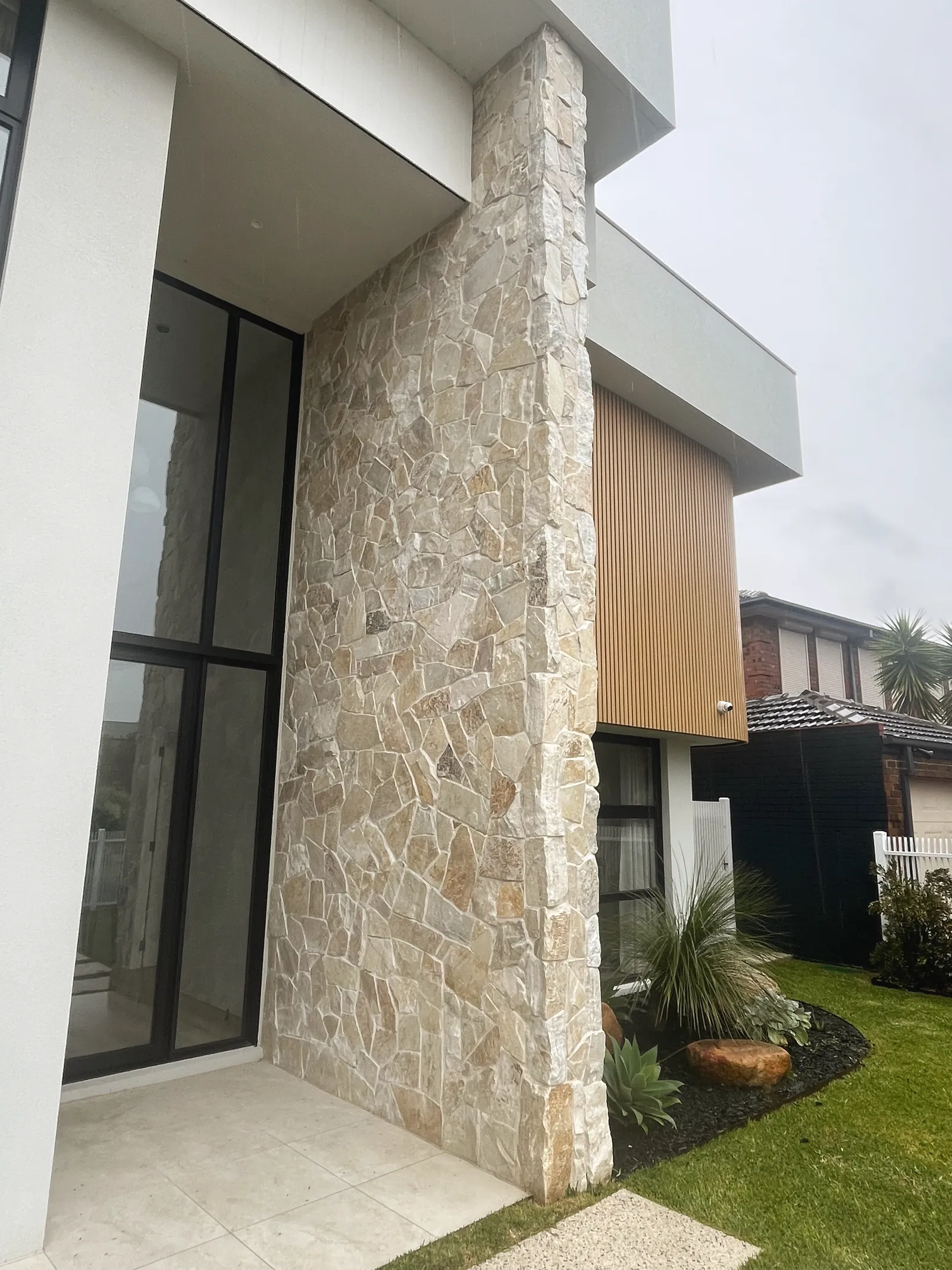 Natural stone cladding running the full height of a modern entry column, next to glazing and timber battens