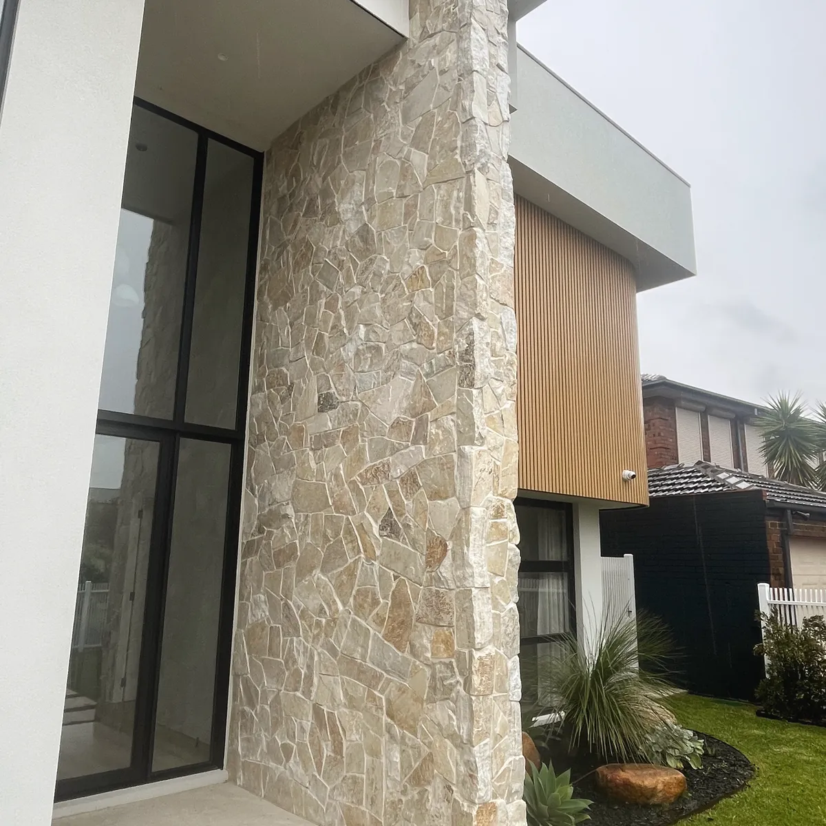 Natural stone cladding running the full height of a modern entry column, next to glazing and timber battens